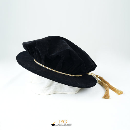 Black velvet hat with gold trim and tassel on a white background.