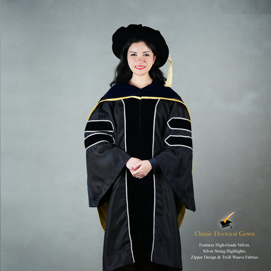 Front view of a person wearing a PhD classic black velvet graduation gown with silver sleeve bars, silver front trim, and a black doctoral bonnet with gold tassel.