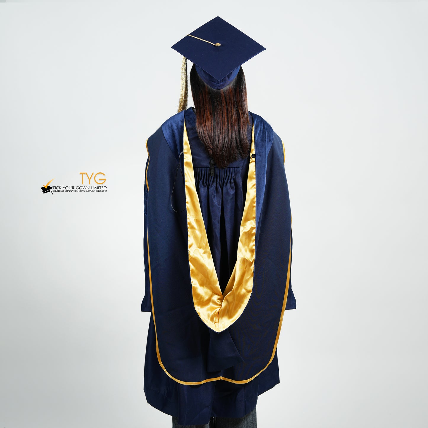 A back view of a person wearing a PhD classic navy blue velvet graduation gown with yellow lining hood, and a navy blue doctoral bonnet with gold tassel.