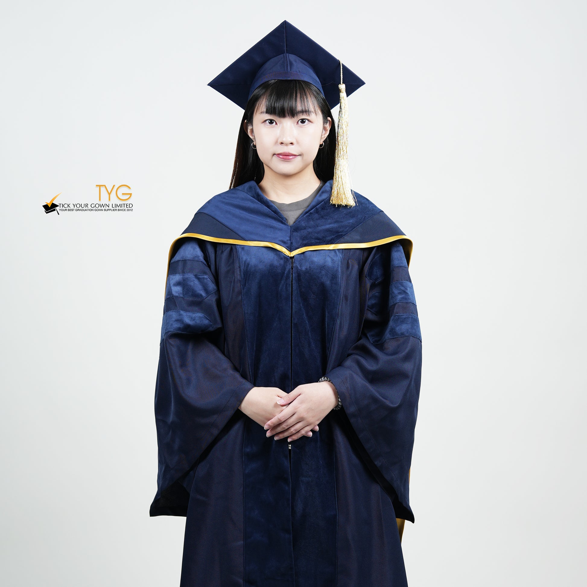 A detailed front view of a person wearing a PhD classic navy blue velvet graduation gown with yellow lining hood, and a navy blue doctoral bonnet with gold tassel.