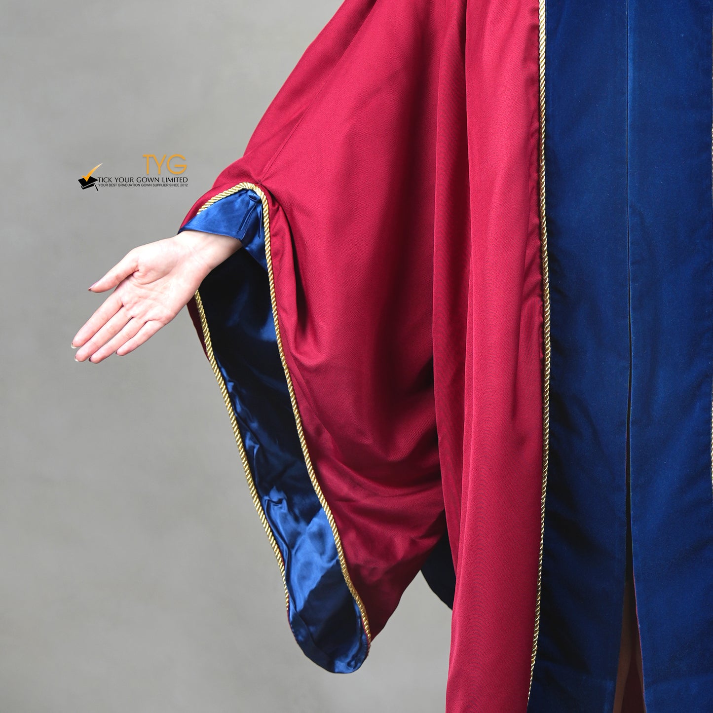 Detailed front view of the arm sleeve of a premium honorary graduation gown in maroon with royal blue inner sleeve lining, royal blue velvet panel, and gold trim.

