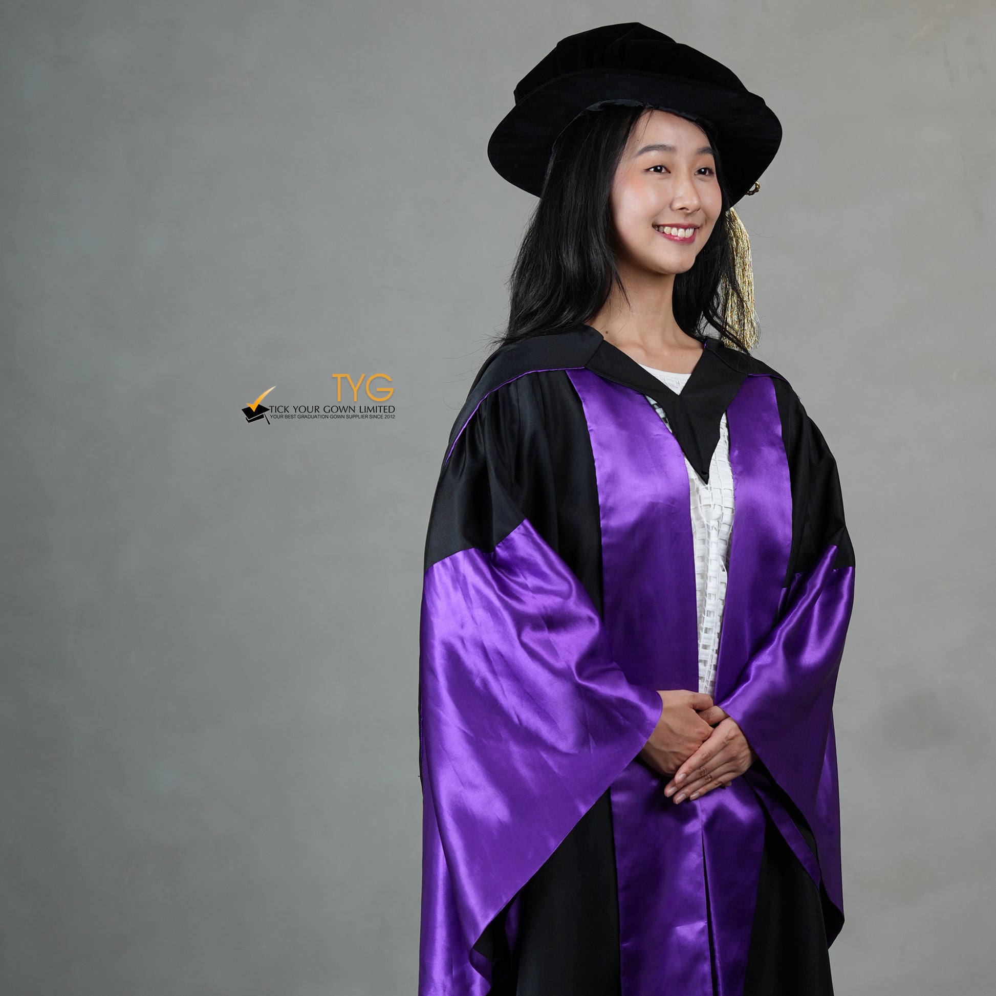 A detailed profile view of a person wearing a graduation gown in black with purple satin panels, matching purple satin sleeve cuffs, and a black doctoral bonnet with gold tassel.