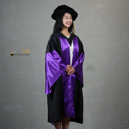 A profile view of a person wearing a graduation gown in black with purple satin panels, matching purple satin sleeve cuffs, and a black doctoral bonnet with gold tassel.