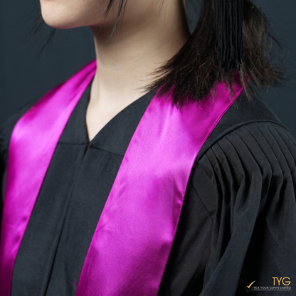 A closeup view of a person wearing a black graduation gown with a pink graduation sash stole on a dark background
