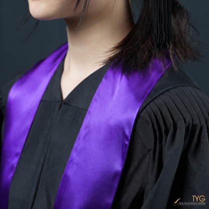 Person wearing a black graduation gown with a purple graduation sash stole on a dark background